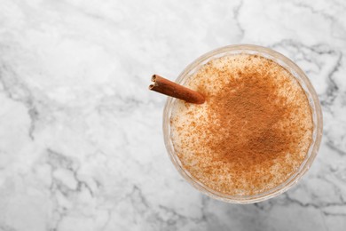 Photo of Delicious eggnog with cinnamon on white marble table, top view. Space for text