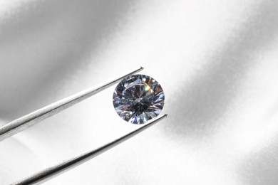 Photo of Tweezers with beautiful shiny diamond on light background, closeup