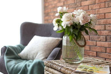 Photo of Vase with beautiful flowers on wicker trunk indoors. Interior decor element