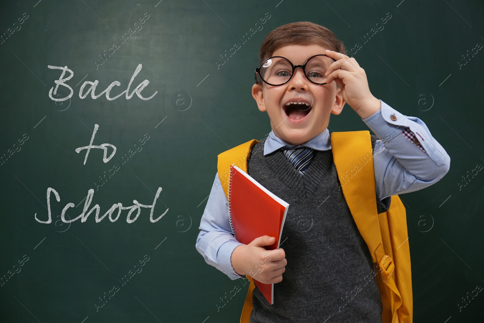 Image of Cute little child wearing glasses near chalkboard with phrase BACK TO SCHOOL