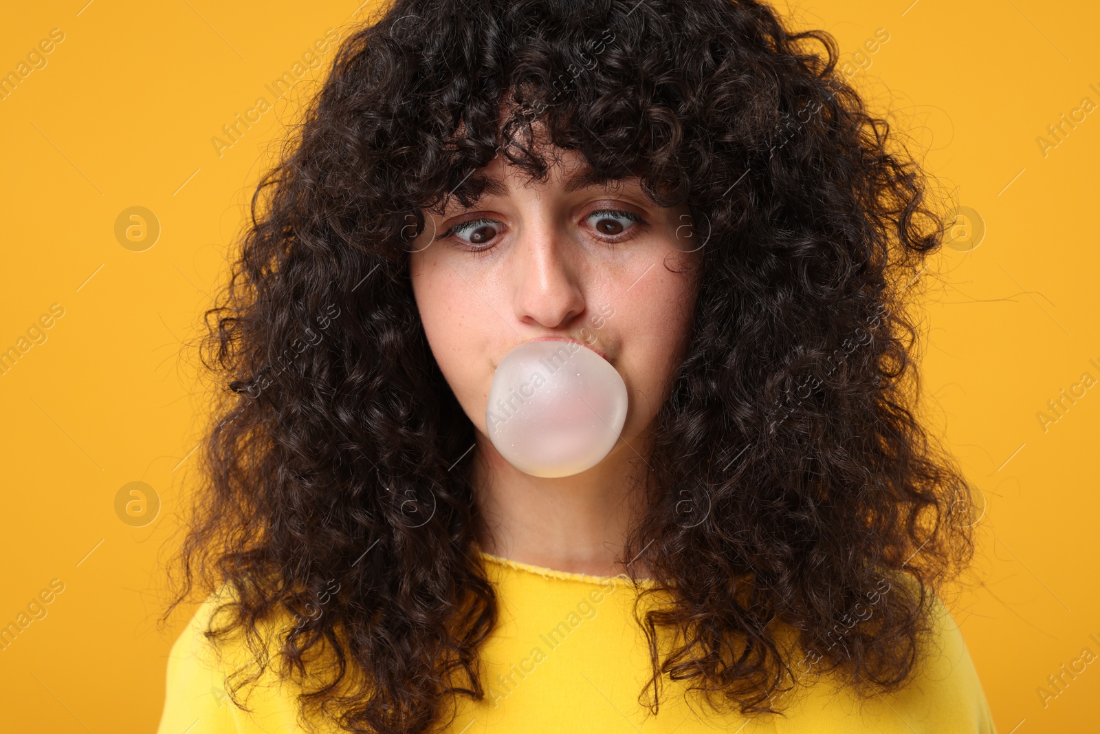 Photo of Beautiful young woman blowing bubble gum on orange background