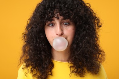 Beautiful young woman blowing bubble gum on orange background