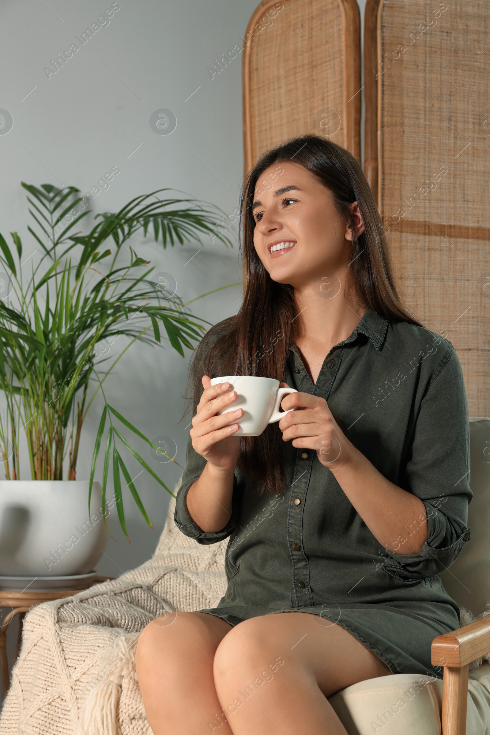 Photo of Happy young woman with cup of coffee sitting in armchair at home
