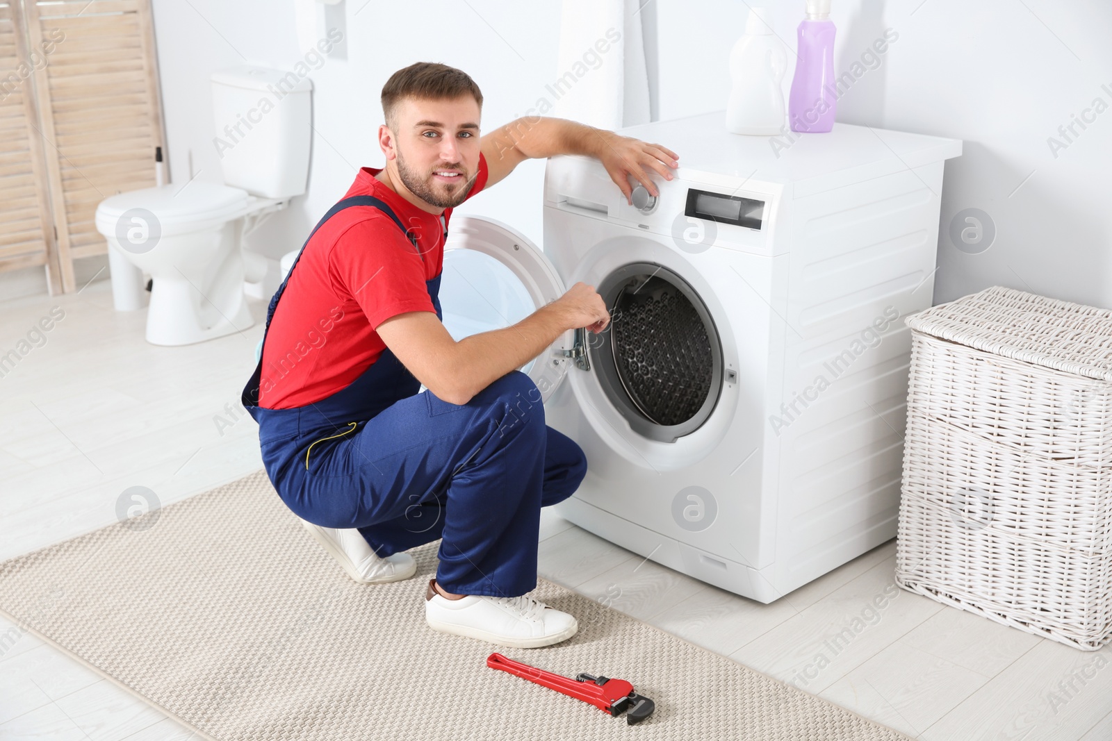 Photo of Young plumber examining washing machine in bathroom