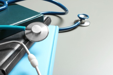 Student textbooks, stethoscopes and space for text on grey background, closeup. Medical education