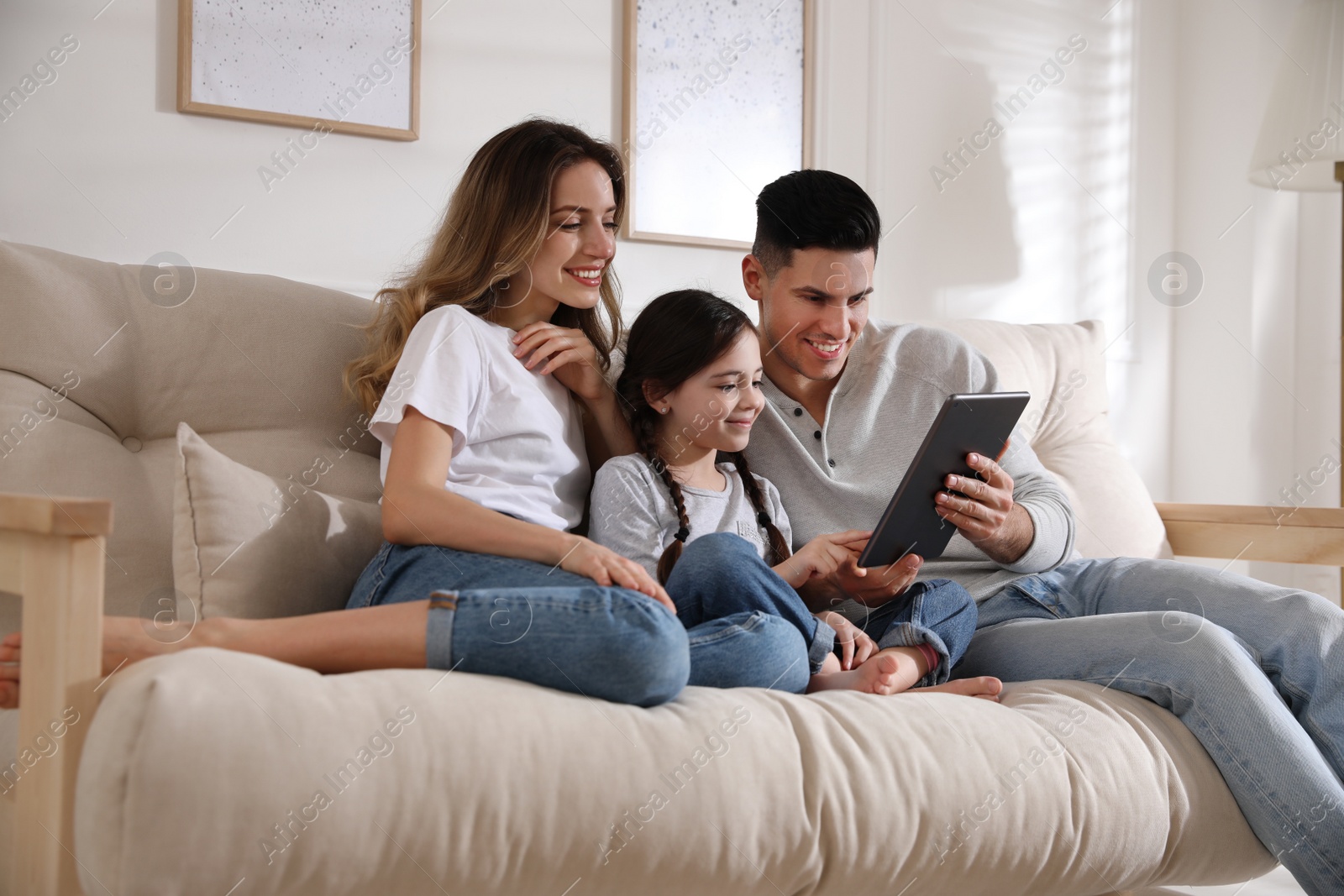 Photo of Happy family with little daughter using tablet on sofa in living room