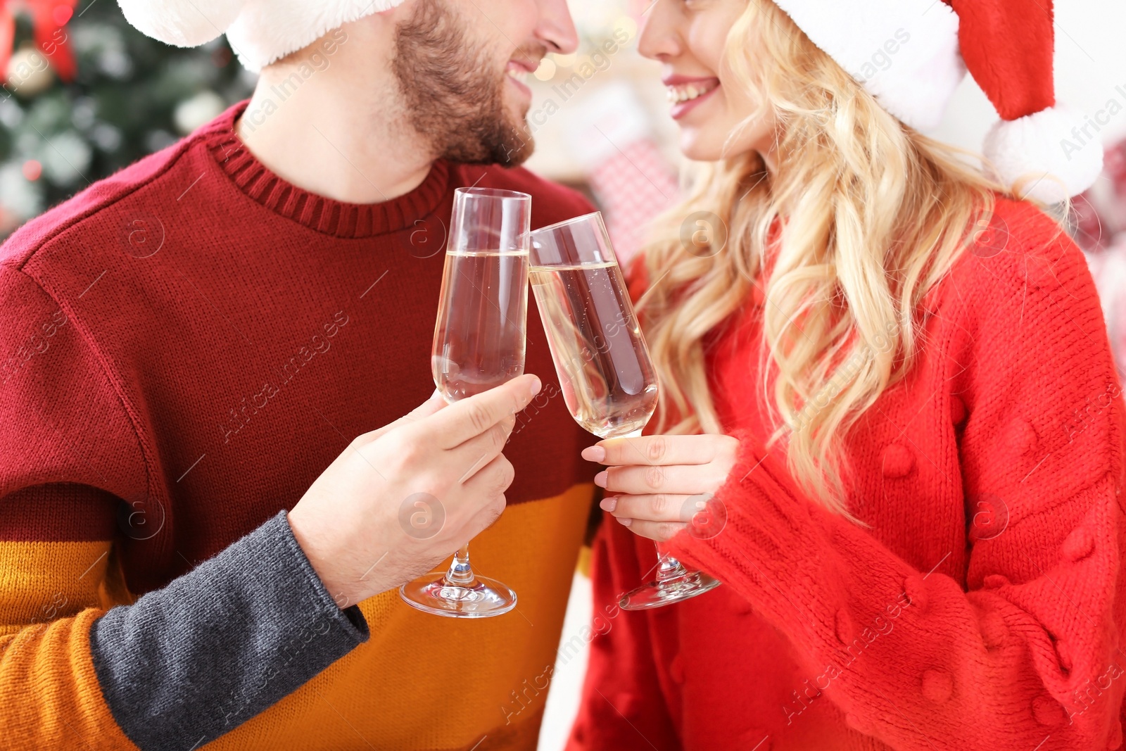 Photo of Young couple in Santa hats with glasses of champagne at home. Christmas celebration