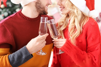 Young couple in Santa hats with glasses of champagne at home. Christmas celebration