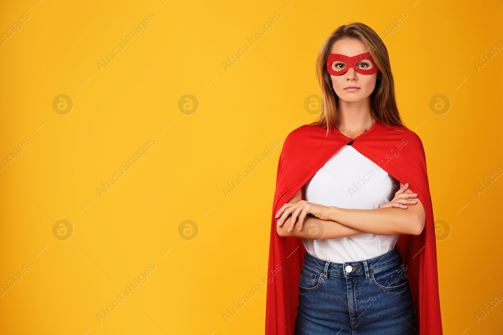 Photo of Confident woman wearing superhero cape and mask on yellow background. Space for text