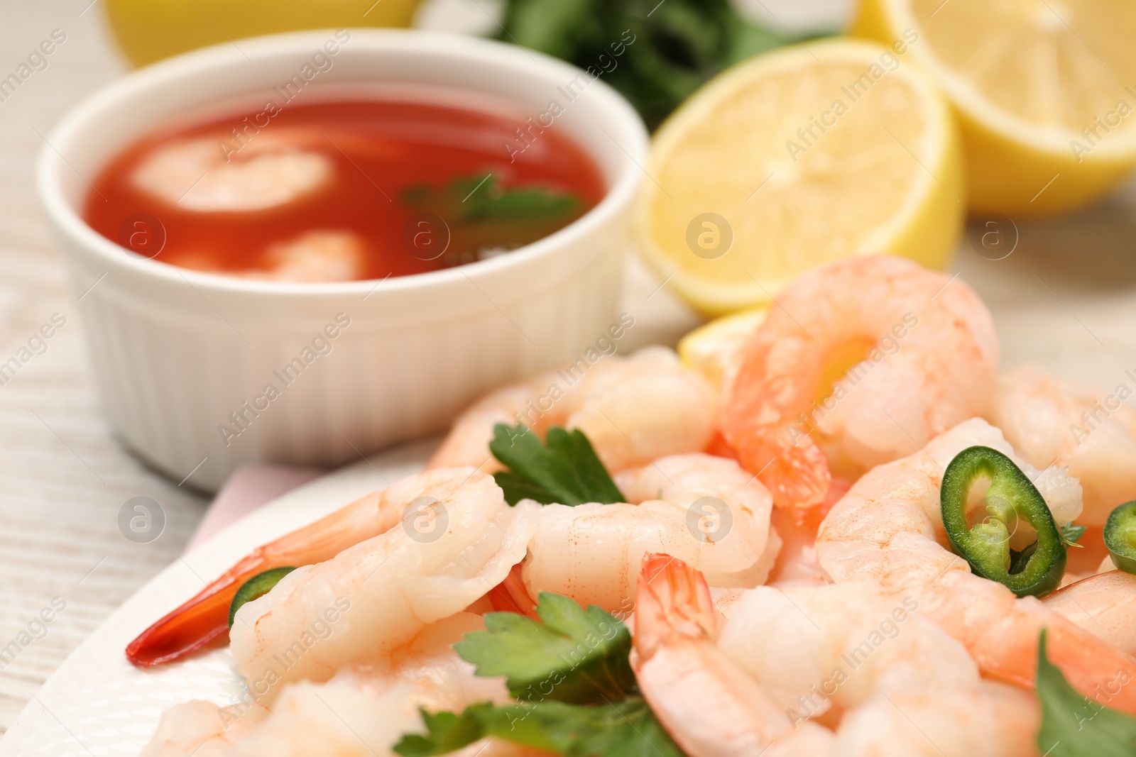 Photo of Tasty boiled shrimps with cocktail sauce, chili and parsley on table, closeup