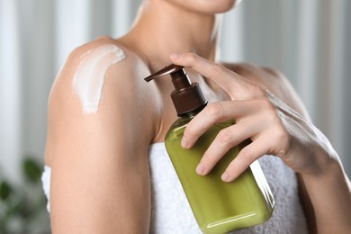 Photo of Woman applying body cream onto shoulder indoors, closeup