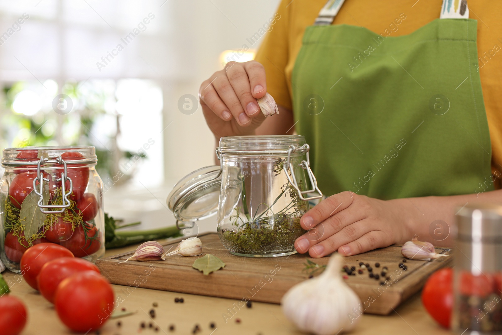 Photo of Woman putting garlic into pickling jar at table in kitchen, closeup