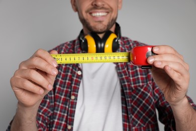 Happy worker holding measuring tape on white background, closeup