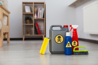 Photo of Bottles of toxic household chemicals with warning signs, brush and scouring sponge in room, space for text