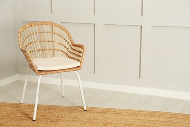 Stylish wicker armchair near light wall in room. Space for text