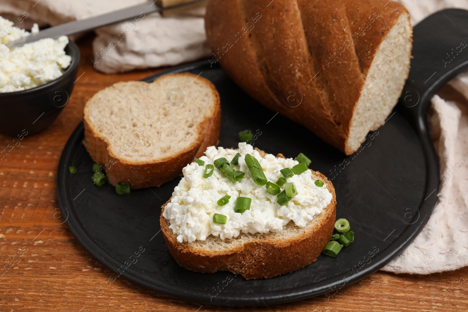 Photo of Bread with cottage cheese and green onion on wooden table, closeup