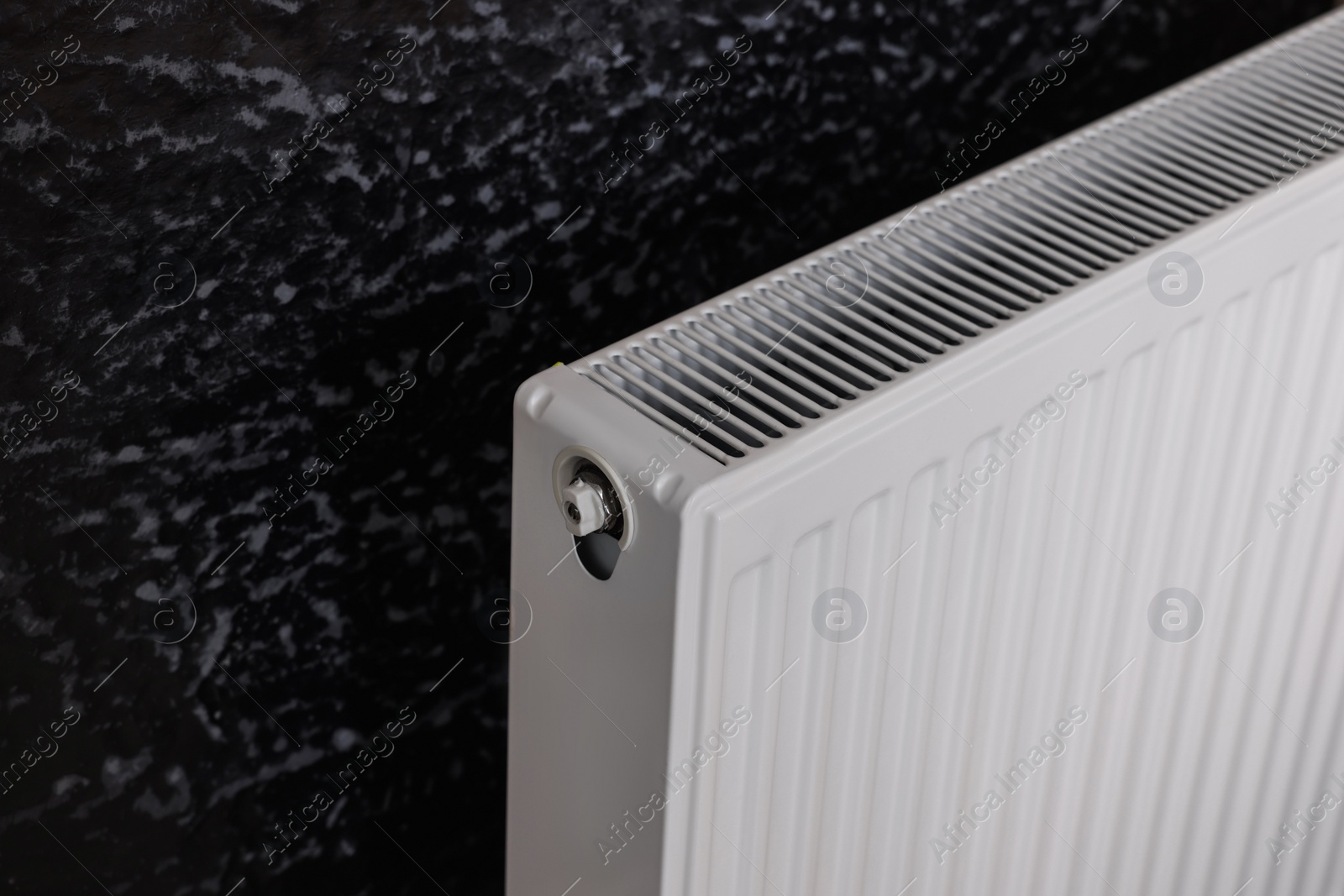 Photo of Modern radiator on black wall, closeup. Central heating system