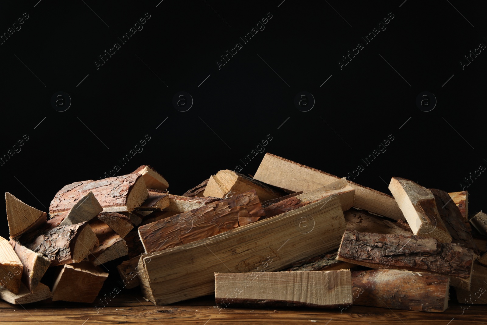 Photo of Cut firewood on table against black background