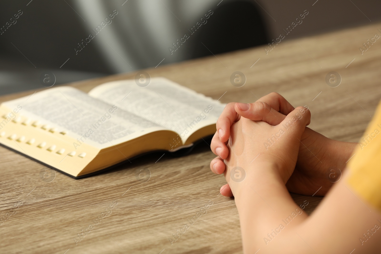 Photo of Religious woman praying over Bible at wooden table indoors, closeup