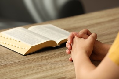 Religious woman praying over Bible at wooden table indoors, closeup