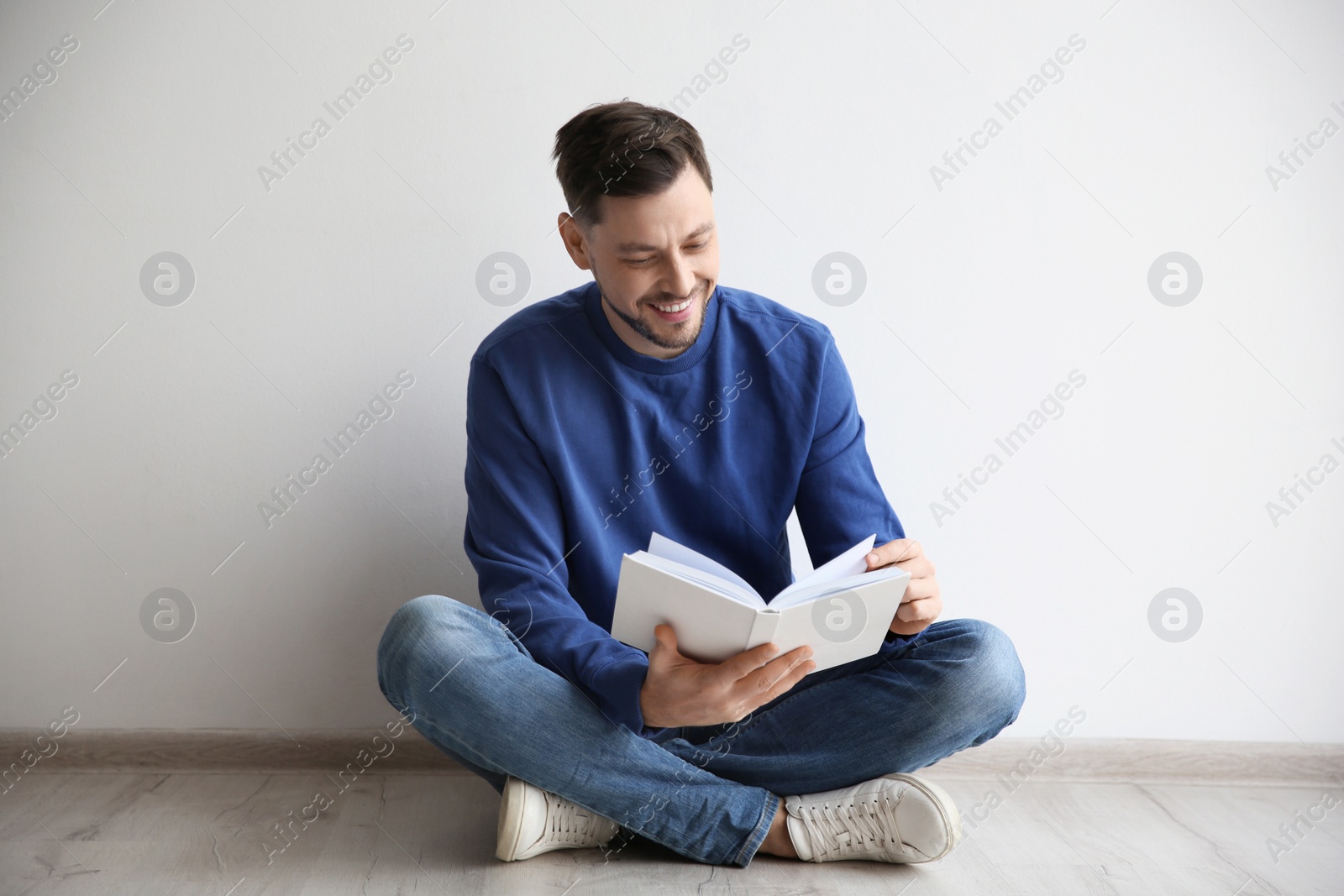 Photo of Handsome man reading book on floor near wall