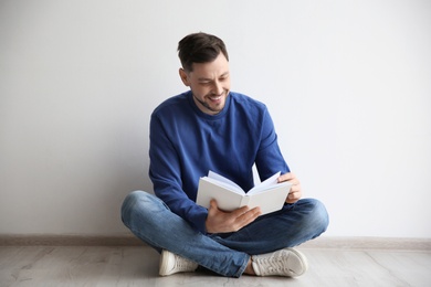 Photo of Handsome man reading book on floor near wall