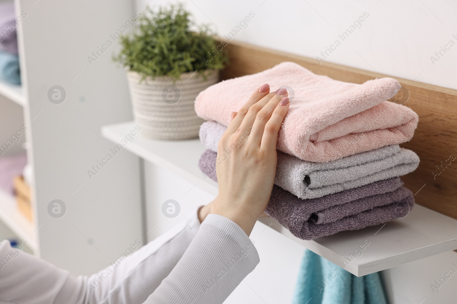 Photo of Woman stacking clean towels on shelf indoors, closeup