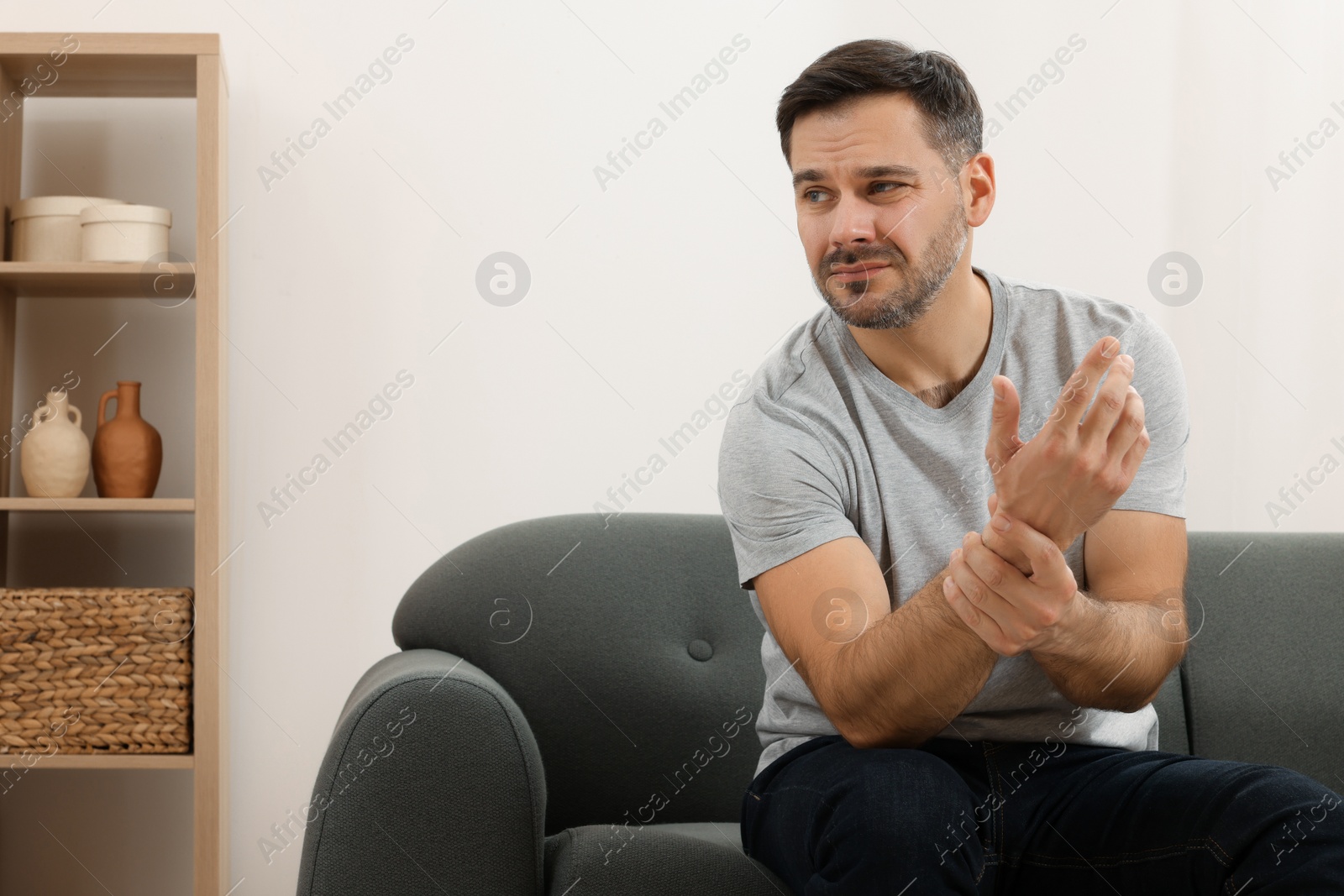 Photo of Man suffering from pain in his hand on sofa indoors. Space for text
