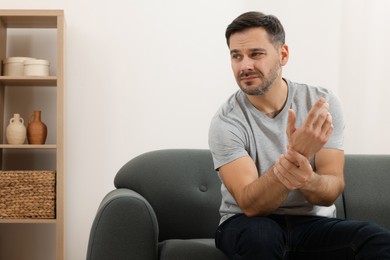 Man suffering from pain in his hand on sofa indoors. Space for text