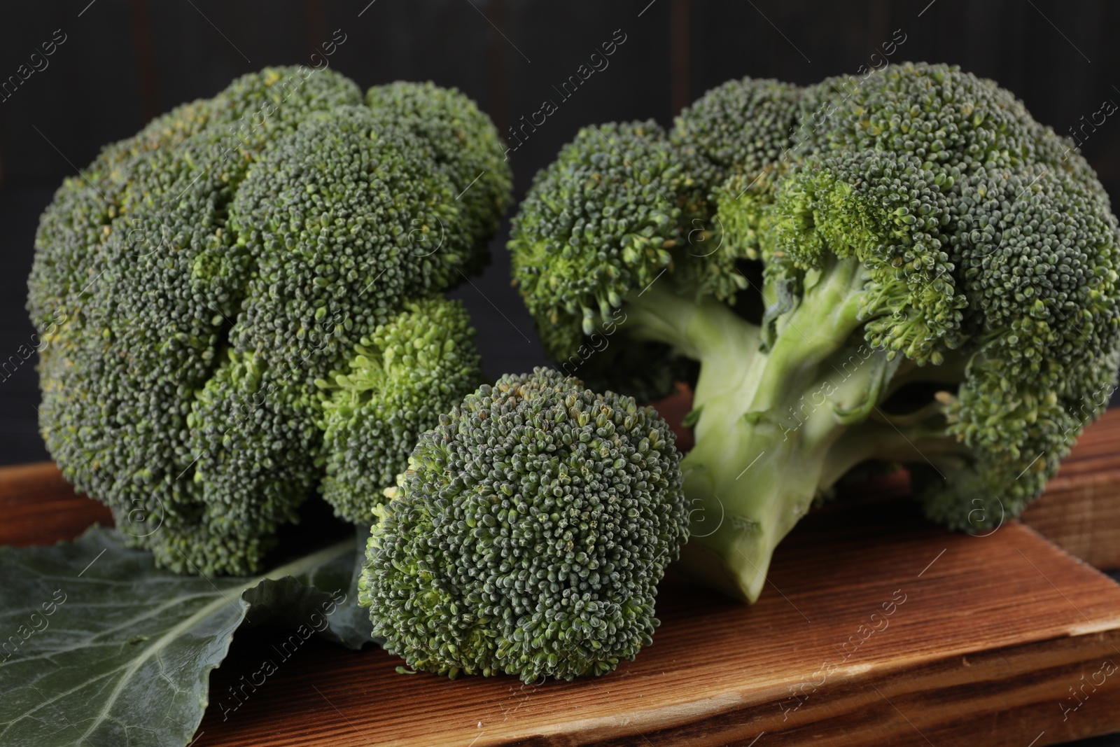 Photo of Wooden board with fresh raw broccoli on table, closeup.