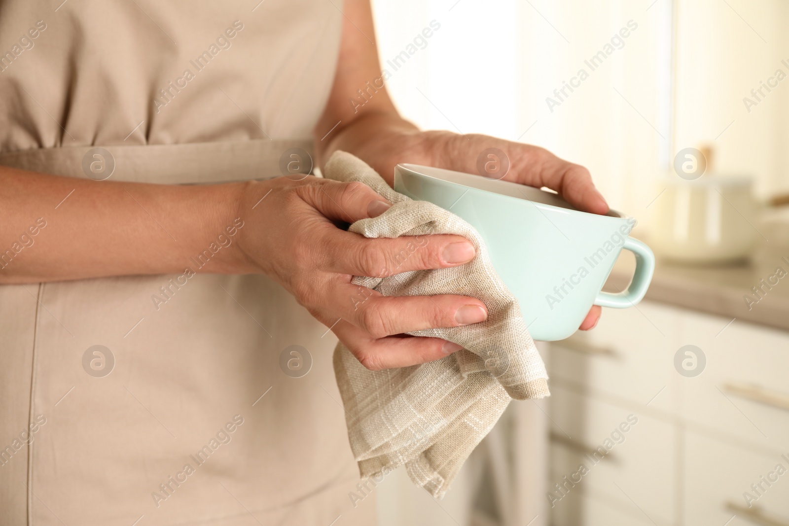 Photo of Woman wiping cup with towel in kitchen, closeup