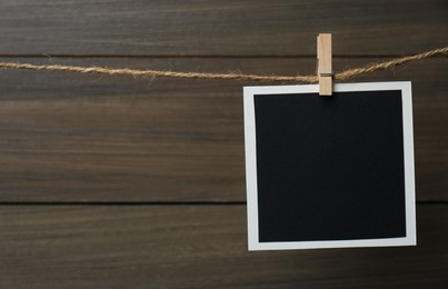 Photo of Clothespin with empty instant frame on twine against wooden background. Space for text