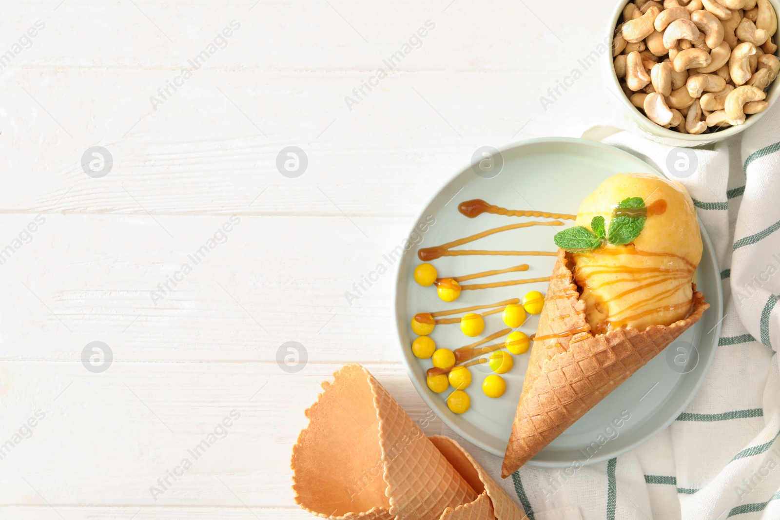 Photo of Flat lay composition with yellow ice cream in wafer cone on white wooden table. Space for text