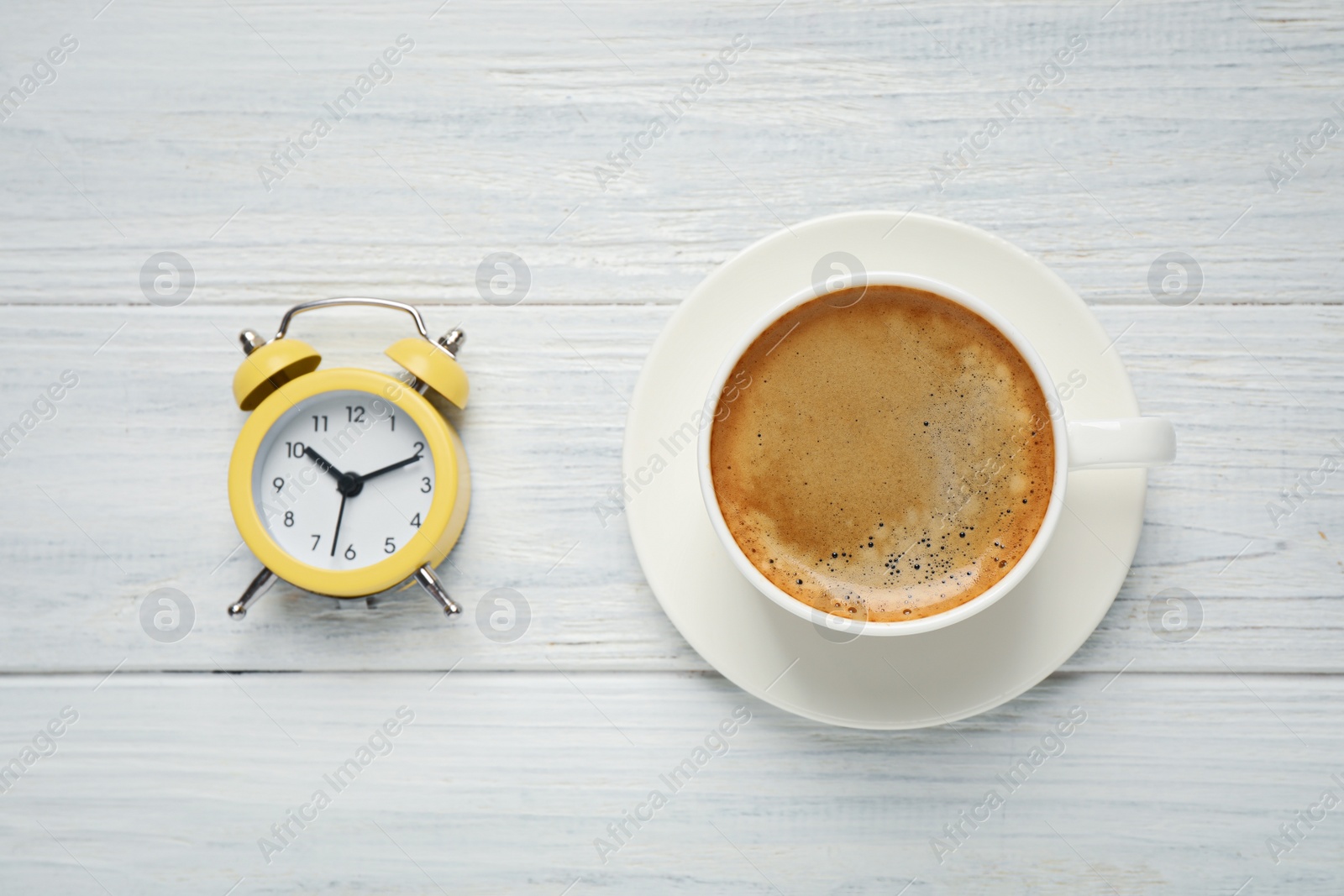 Photo of Cup of morning coffee and alarm clock on white wooden table, flat lay