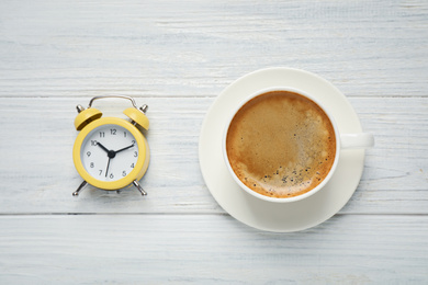 Photo of Cup of morning coffee and alarm clock on white wooden table, flat lay