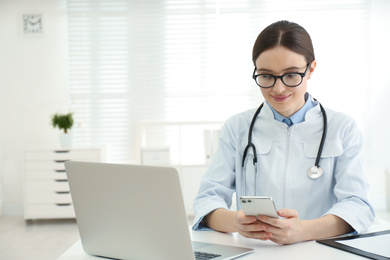 Photo of Young female doctor with smartphone at table in office