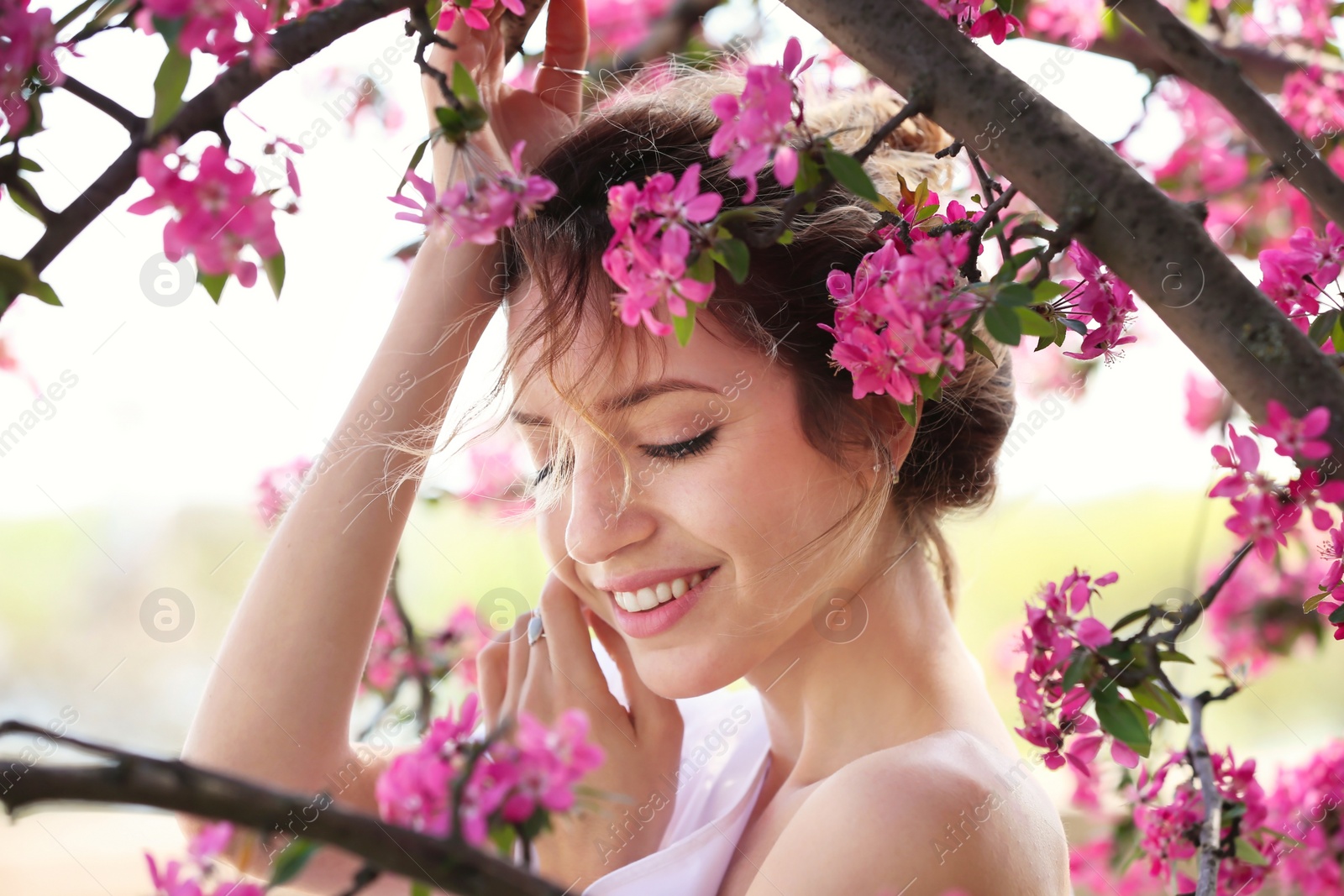 Photo of Attractive young woman posing near blossoming tree on sunny spring day