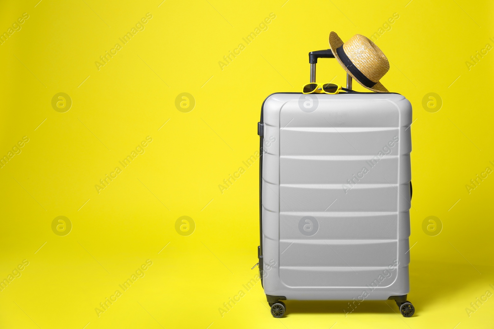 Photo of Stylish grey suitcase with hat and sunglasses on yellow background. Space for text