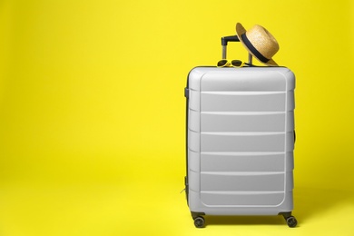 Photo of Stylish grey suitcase with hat and sunglasses on yellow background. Space for text