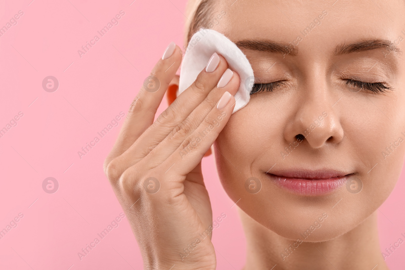 Photo of Beautiful woman removing makeup with cotton pad on pink background, closeup. Space for text