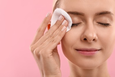 Photo of Beautiful woman removing makeup with cotton pad on pink background, closeup. Space for text