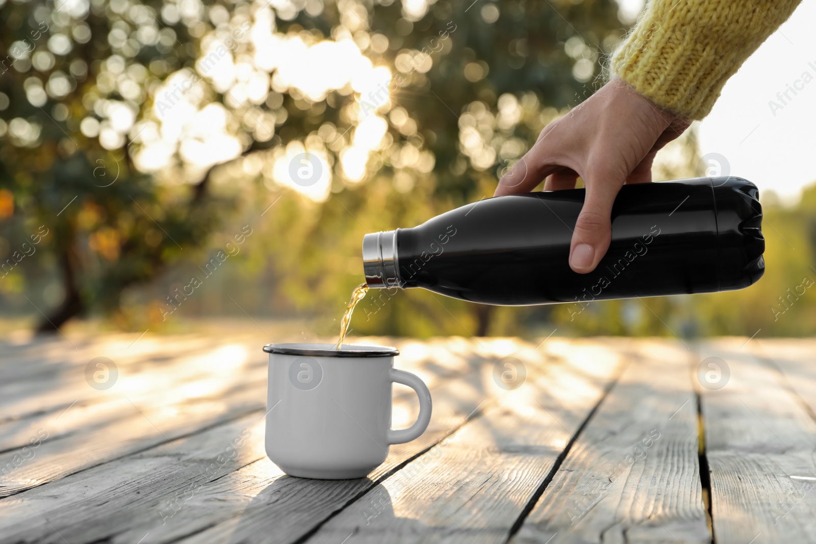 Photo of Woman pouring hot drink from thermos bottle into cup outdoors, closeup