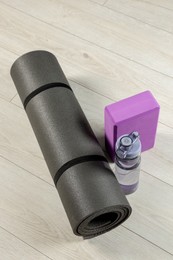 Exercise mat, yoga block and bottle of water on light wooden floor, above view