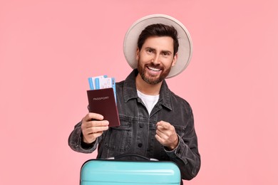 Smiling man pointing at passport and tickets on pink background