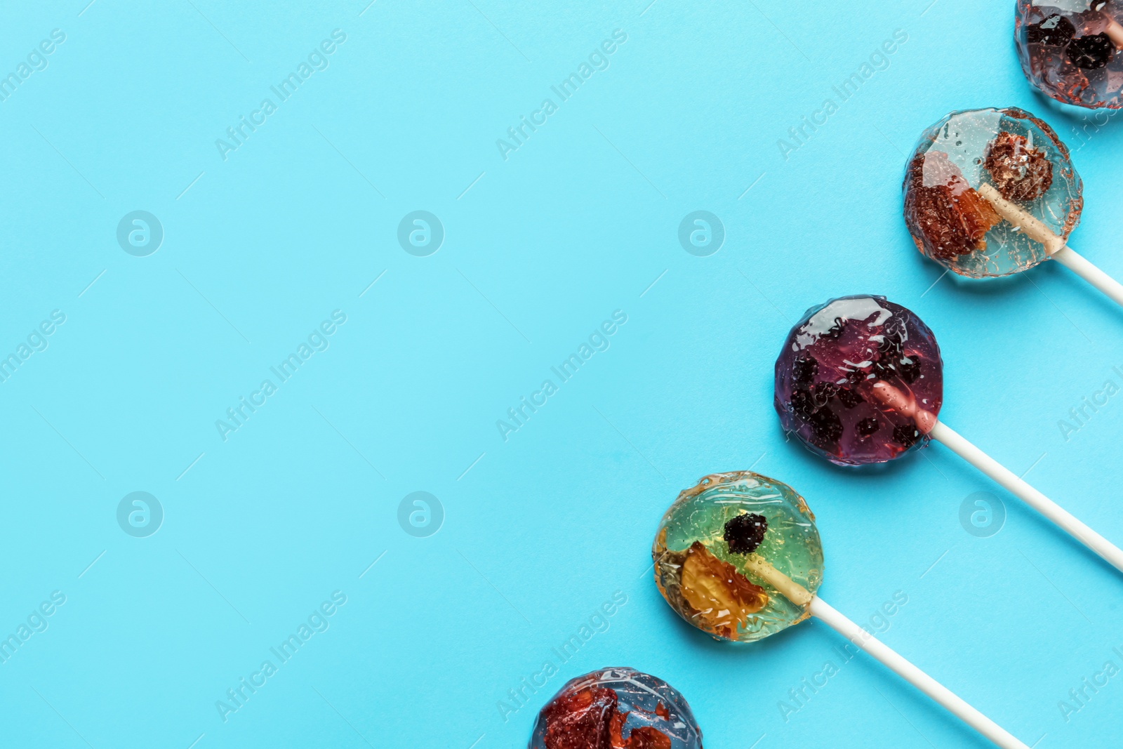 Photo of Sweet colorful lollipops with berries on light blue background, flat lay. Space for text