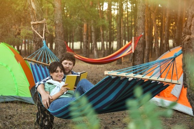 Photo of Lovely couple with book resting in comfortable hammock outdoors