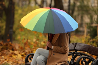 Photo of Woman with rainbow umbrella sitting on bench in autumn park
