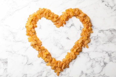 Photo of Heart shaped frame of raisins and space for text on marble background. Dried fruit as healthy snack