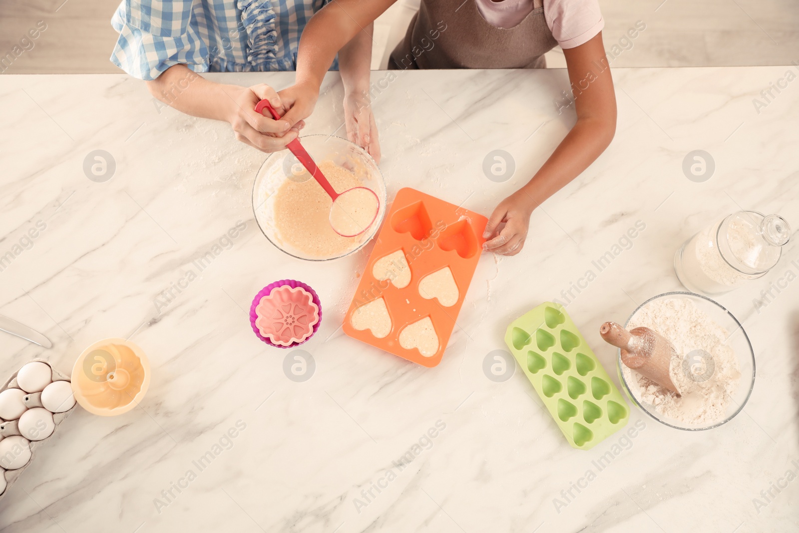 Photo of Mother and daughter making cupcakes together in kitchen, top view