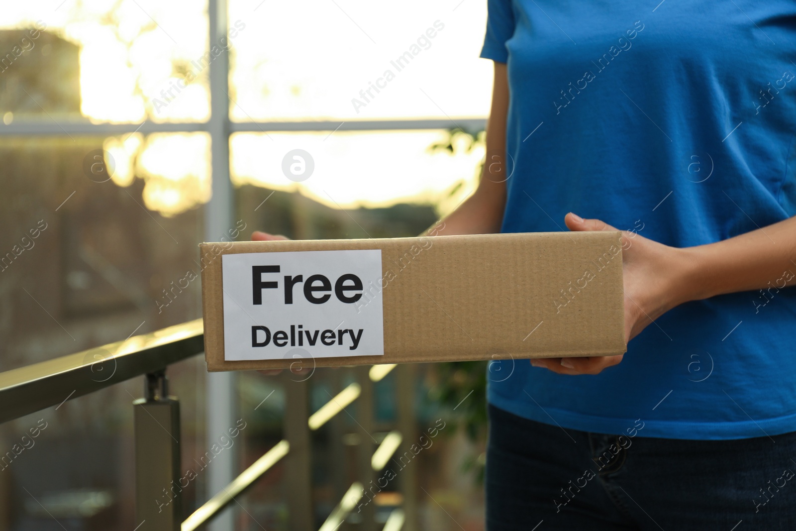 Photo of Courier holding parcel with sticker Free Delivery indoors, closeup